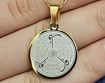 Può includere: Collana con catena dorata e ciondolo rotondo con calligrafia araba in bianco e nero su sfondo bianco.