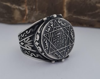 May include: A silver ring with an intricate design featuring a star of David and Arabic script. The ring has a wide band with a decorative pattern.
