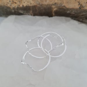 May include: A cluster of silver-colored rings with irregular, petal-like edges. The rings are interlocked, creating a layered effect. The jewelry is set against a white background.