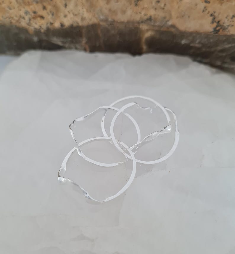 May include: A cluster of silver-colored rings with irregular, petal-like edges. The rings are interlocked, creating a layered effect. The jewelry is set against a white background.