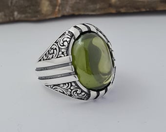 Puede incluir: Un anillo de plata con una piedra preciosa verde ovalada engastada en una banda de plata detallada.