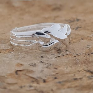 May include: A silver ring with a woven design. The ring features a series of interwoven bands, creating a textured and intricate pattern. The polished metal reflects light, highlighting the details of the design. The ring is a piece of jewelry.