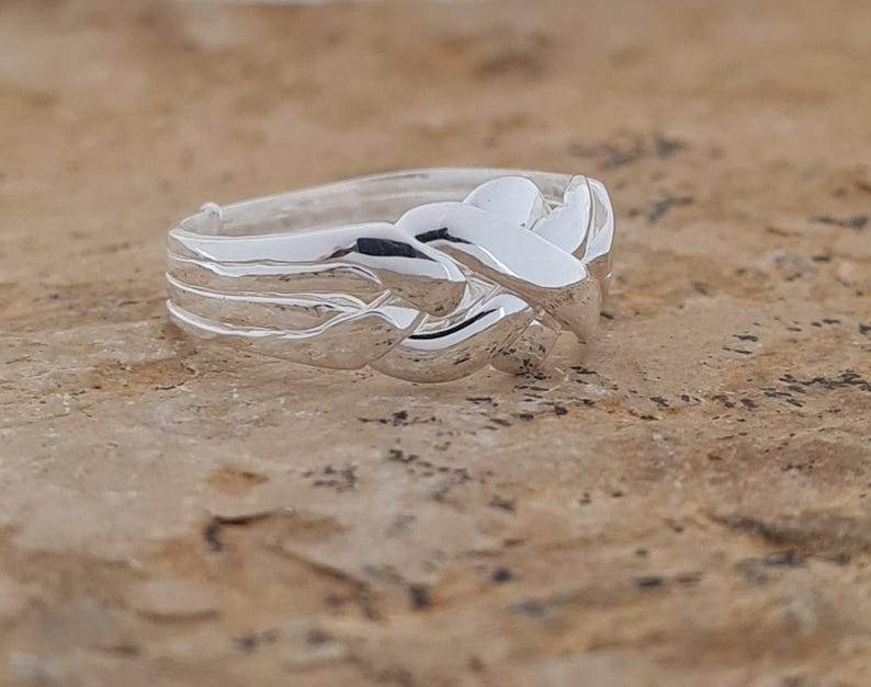 May include: A silver ring with a woven design. The ring features a series of interwoven bands, creating a textured and intricate pattern. The polished metal reflects light, highlighting the details of the design. The ring is a piece of jewelry.