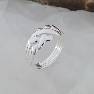 May include: A silver puzzle ring with an interwoven design. The ring features multiple bands and interlocking pieces, creating a complex and intriguing appearance. The polished metal reflects light, highlighting the intricate details of the design.