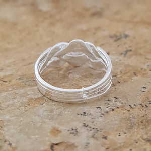May include: A silver ring with a woven design. The ring features a series of interwoven strands, creating a textured surface. The ring is set against a neutral background, highlighting its intricate details and craftsmanship.