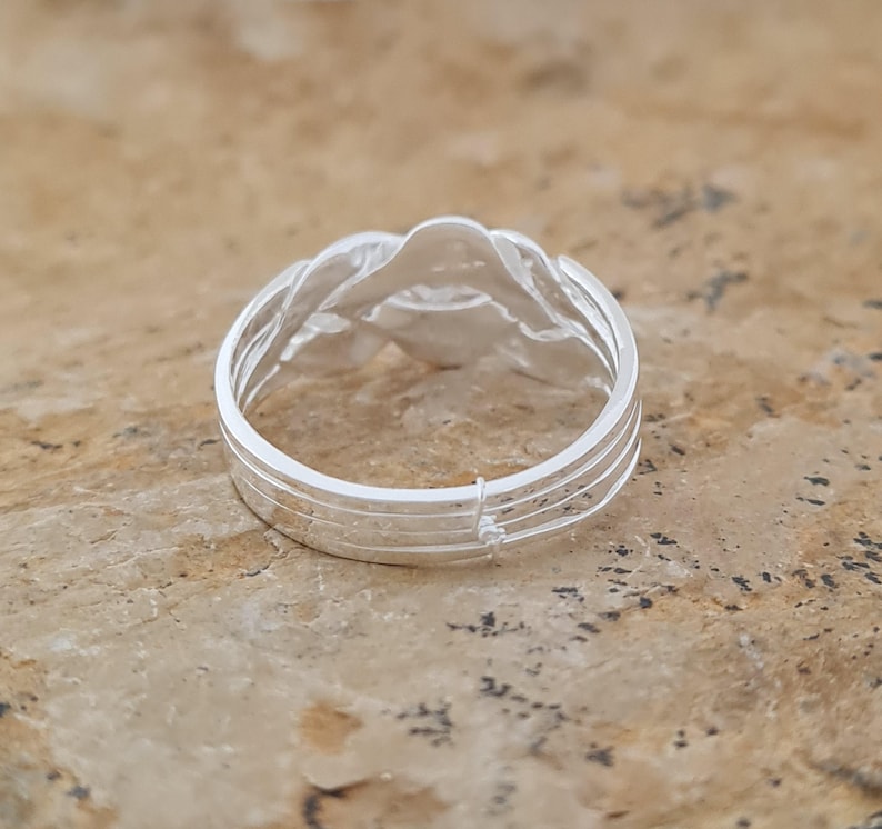 May include: A silver ring with a woven design. The ring features a series of interwoven strands, creating a textured surface. The ring is set against a neutral background, highlighting its intricate details and craftsmanship.