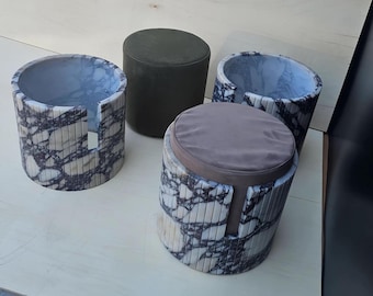 May include: Four cylindrical stools. Two are made of marble-like material with gray and white veining. One has a gray cushion. The other is a solid dark green. The stools have a modern design.