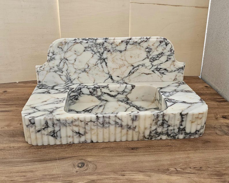 May include: A marble sink with a rectangular basin and a decorative back. The sink is white with black and gray veining. The front of the sink has vertical ribbed detailing.