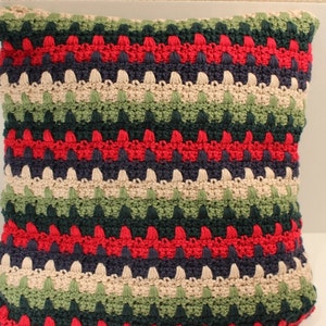 May include: A striped crocheted pillow with red, green, blue, and beige yarn. The pillow is made with a textured stitch that creates a bumpy surface.