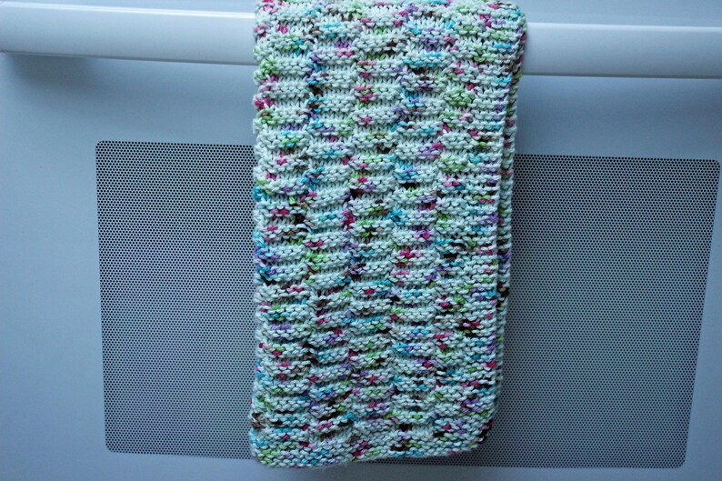 May include: A white knitted dishcloth with a textured pattern and multicolored flecks of pink, green, blue, and brown.