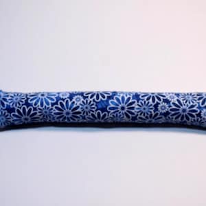May include: A long, cylindrical fabric tube featuring a repeating pattern of white daisy-like flowers on a deep blue background. The ends of the fabric are stitched closed, creating a straight, elongated shape with a soft, textured appearance.