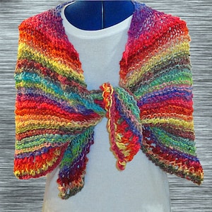 May include: A colorful crocheted shawl with a rainbow pattern. The shawl is tied in a knot at the neck and has a fringed edge.