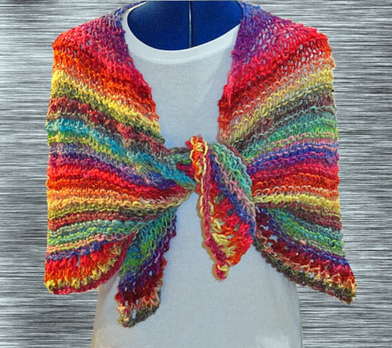 May include: A colorful crocheted shawl with a rainbow pattern. The shawl is tied in a knot at the neck and has a fringed edge.