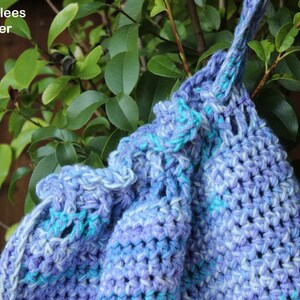 Puede incluir: Bolso de ganchillo hecho a mano en tonos azules y morados, con cierre de cord&oacute;n y un patr&oacute;n de puntada texturizada. El bolso cuelga de una rama de &aacute;rbol, con el texto "Kimberlees Korner" visible.