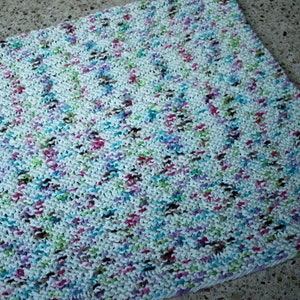 May include: A white knitted dishcloth with a multi-colored yarn pattern. The yarn is a mix of pink, blue, green, brown, and white.