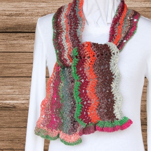 May include: A multi-colored crocheted scarf with a scalloped edge. The scarf is made with a variety of shades of red, orange, green, brown, and pink yarn.