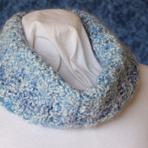 May include: A blue and white knitted cowl neck scarf. The scarf is made of a soft, fluffy yarn and has a loose, drapey style.