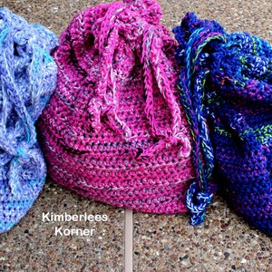 Puede incluir: Tres bolsas de crochet hechas a mano con cord&oacute;n en tonos de azul, rosa y morado. Las bolsas est&aacute;n hechas con hilo grueso y tienen un aspecto texturizado. El texto "Kimberlees Korner" es visible en la parte inferior izquierda de la imagen.