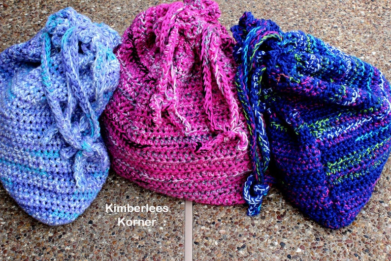 Puede incluir: Tres bolsas de crochet hechas a mano con cord&oacute;n en tonos de azul, rosa y morado. Las bolsas est&aacute;n hechas con hilo grueso y tienen un aspecto texturizado. El texto "Kimberlees Korner" es visible en la parte inferior izquierda de la imagen.