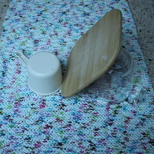 May include: A white plastic measuring cup, a wooden cutting board, and a clear glass jar on a colorful knitted kitchen towel.