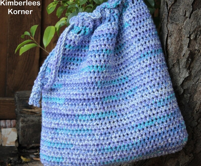 Puede incluir: Un bolso de ganchillo hecho a mano con cord&oacute;n en tonos azules y morados. El bolso presenta un patr&oacute;n de puntadas texturizadas y una parte superior fruncida con cierre de cord&oacute;n. El bolso est&aacute; hecho de hilo suave y es adecuado para llevar varios art&iacute;culos.