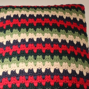 May include: A multi-colored crocheted pillow with a chevron pattern in shades of green, red, cream, and navy blue.