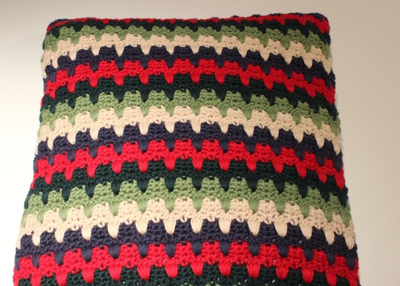 May include: A multi-colored crocheted pillow with a chevron pattern in shades of green, red, cream, and navy blue.