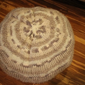 Könnte beinhalten: Ein runder, gestrickter Hocker mit einem weißen und grauen geometrischen Muster. Der Hocker ist aus weichem, flauschigem Garn gefertigt und hat eine runde Form.