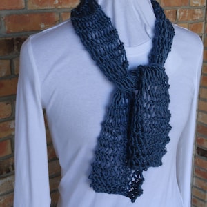 May include: A blue knitted scarf with a loose, open weave. The scarf is tied in a knot around the neck.