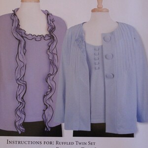May include: A two-piece set of clothing, one a lavender blouse with a ruffled neckline and a matching lavender cardigan with buttons. The cardigan has a pleated design.