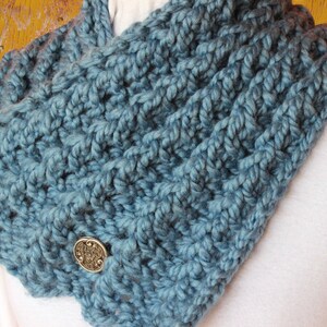 Puede incluir: Una bufanda infinita de crochet azul turquesa con dos botones metálicos decorativos.