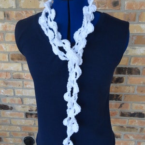 May include: White crocheted scarf with a delicate, lacy design. The scarf is draped over a blue mannequin and is long enough to be worn as a necklace or a shawl.