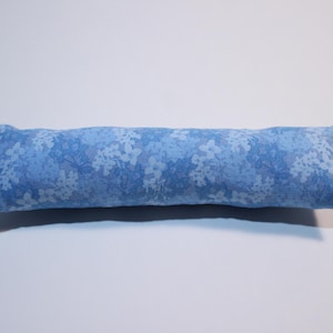 May include: A long, rectangular bolster pillow featuring a light blue fabric with a repeating pattern of small, darker blue floral blossoms. The pillow has a soft, stuffed appearance with stitched ends and a consistent cylindrical shape throughout.