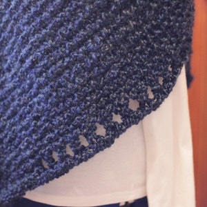 May include: A close-up of a dark blue knitted shawl with a textured pattern. The shawl has a scalloped edge with decorative holes. The garment is draped over a white shirt.