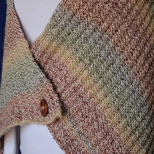 Op de afbeelding: Een veelkleurige gebreide sjaal met een bruine knoop. De sjaal is gemaakt van zacht, getextureerd garen en heeft een diagonaal patroon.