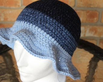 Può includere: Un cappello da sole in crochet blu e bianco con un'ampia tesa. Il cappello è realizzato con un gradiente di filato blu, che inizia con un blu scuro in cima e sfuma in un blu chiaro sul bordo.