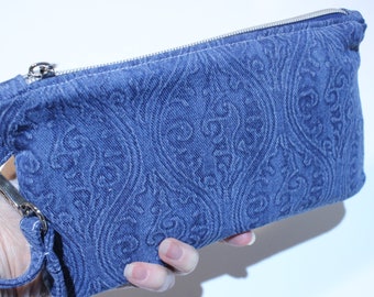 Pode incluir: Uma clutch de ganga azul com um padrão paisley e um fecho de correr prateado. A clutch tem uma alça destacável.
