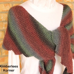 May include: A hand-knitted shawl in shades of red, green, and gray, draped over a white top. The shawl features a textured stitch pattern and a scalloped edge. The text "Kimberlees Korner" is visible in the lower left corner.