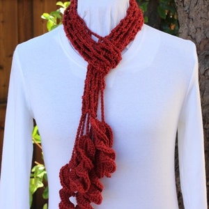 May include: A red crocheted scarf with a unique, textured design. The scarf is made of a soft, lightweight yarn and features a long, flowing fringe.