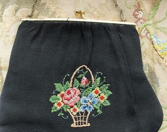Pode incluir: Uma bolsa de noite de tecido preto com uma alça de corrente dourada e um design de bordado floral. O bordado apresenta uma cesta de flores em tons de rosa, azul, amarelo e verde.