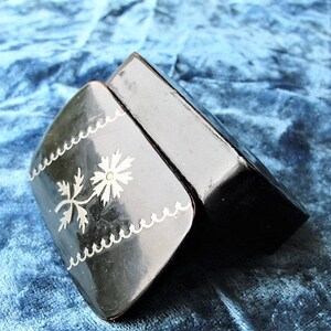 May include: A small black box with a silver floral design on the lid. The box is closed and the lid is slightly ajar.