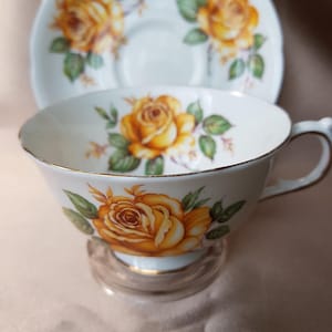 Peut inclure: Une tasse à thé et une soucoupe blanches avec un motif de roses jaunes. La tasse et la soucoupe ont une bordure dorée.