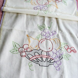 May include: White linen tea towel with embroidered fruit and a basket. The fruit includes pears, grapes, and cherries in shades of red, purple, green, and yellow.