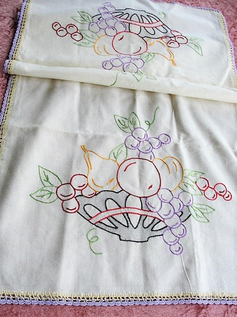 May include: White linen tea towel with embroidered fruit and a basket. The fruit includes pears, grapes, and cherries in shades of red, purple, green, and yellow.
