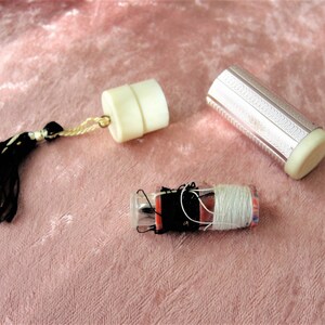 May include: Three vintage sewing kits with white and silver metal cases. One kit has a black and white tassel. The kits contain thread, needles, and other sewing supplies.