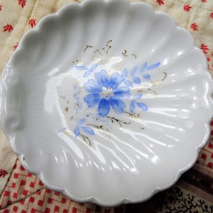 May include: A white porcelain dish with a scalloped edge and a blue and gold floral design. The dish is perfect for holding jewelry or other small items.