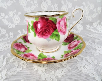 May include: A white teacup and saucer with a pink and red rose pattern and gold trim.