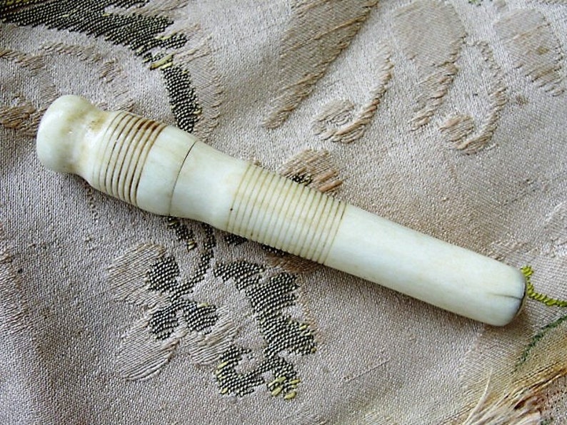 May include: A white, bone-like, ribbed, cylindrical object with a rounded end. The object is lying on a beige fabric with a floral pattern.