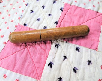 May include: A wooden thimble with a natural finish. The thimble is closed on one end and open on the other. It is lying on a pink and white patchwork quilt.