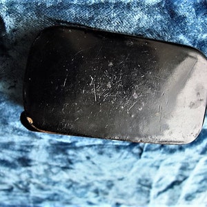 May include: A black rectangular box with a smooth, slightly textured surface. The box has a slightly rounded edge and appears to be made of a hard material.